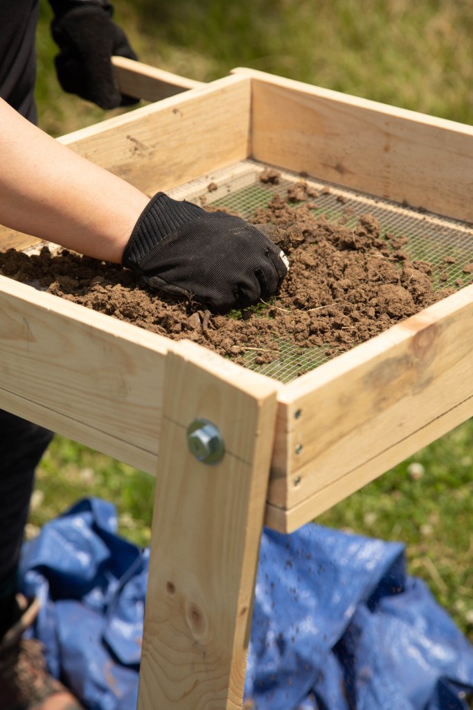 Someone sifts dirt using a mesh screen.