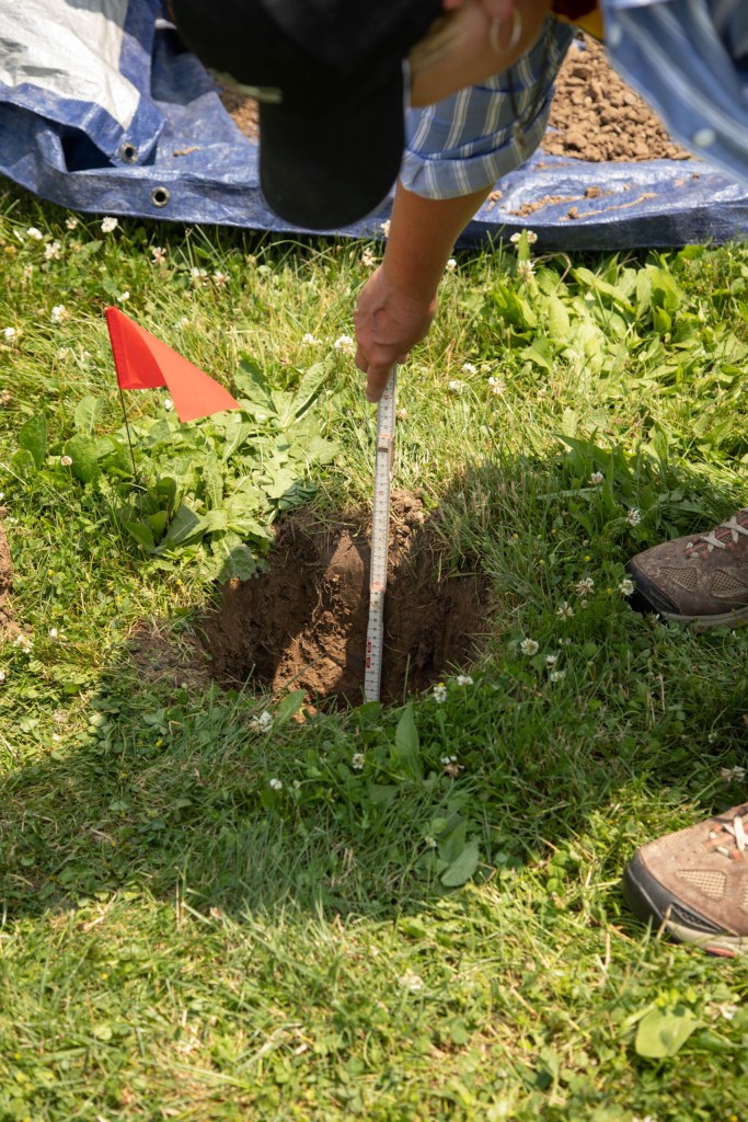 A man measures how deep a dug hole goes.